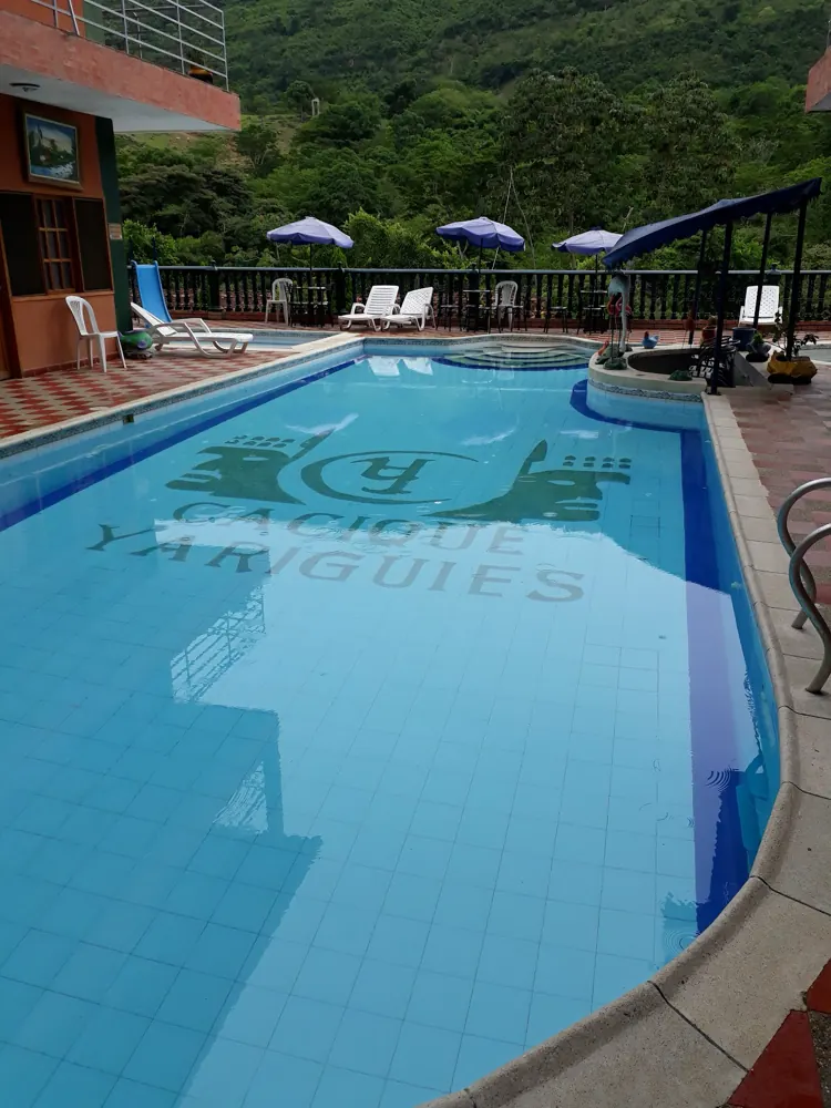 Piscina grande del hotel con el escudo en el fondo y sombrillas alrededor