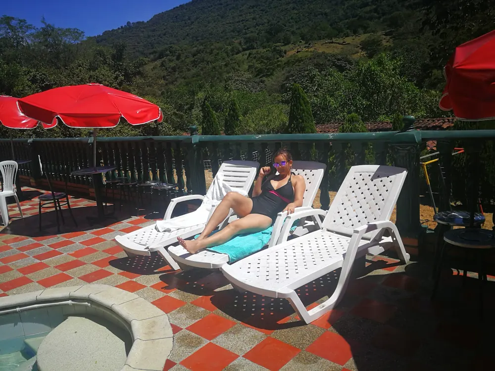 Camas de sol blancas con sombrilla roja y montaña verde de fondo